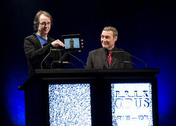 Pierre Alexandre Tremblay (on the screen of an iPad held up by Jean-François Denis) receiving the Prix Opus 2010-11 “Album of the year — actuelle and electroacoustic musics” at the 15th Gala des Prix Opus at Salle Bourgie in Montréal. The host of the event is Mario Paquet (on the right side) [Photo: CQM, Montréal (Québec), January 29, 2012]